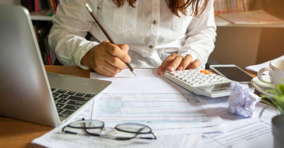 Woman calculating house building costs with calculator and documents in an office setting.