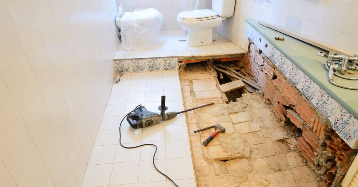 Bathroom under renovation showing exposed flooring and tools for remodeling.