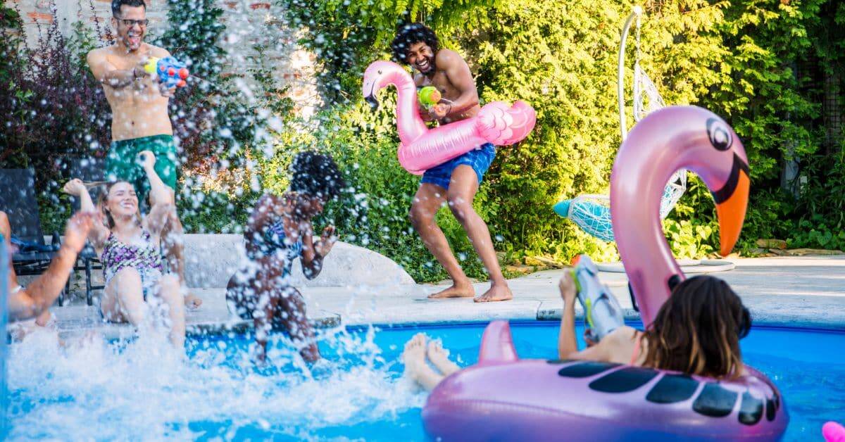Family enjoying a lively pool party with kids playing and floating inflatables on a sunny day.