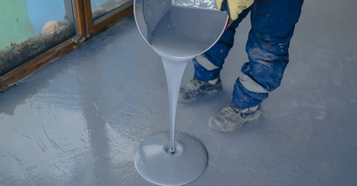 Worker pouring epoxy resin onto a floor for a durable coating.
