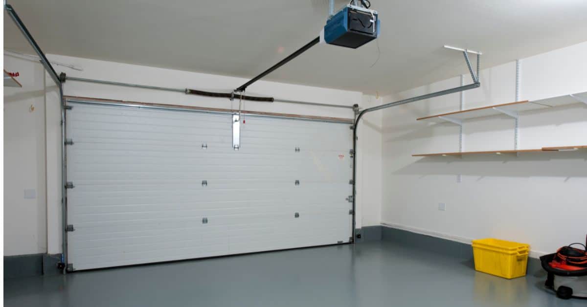 Garage interior featuring a large white sectional door, organized shelving, and a clean, spacious fl.