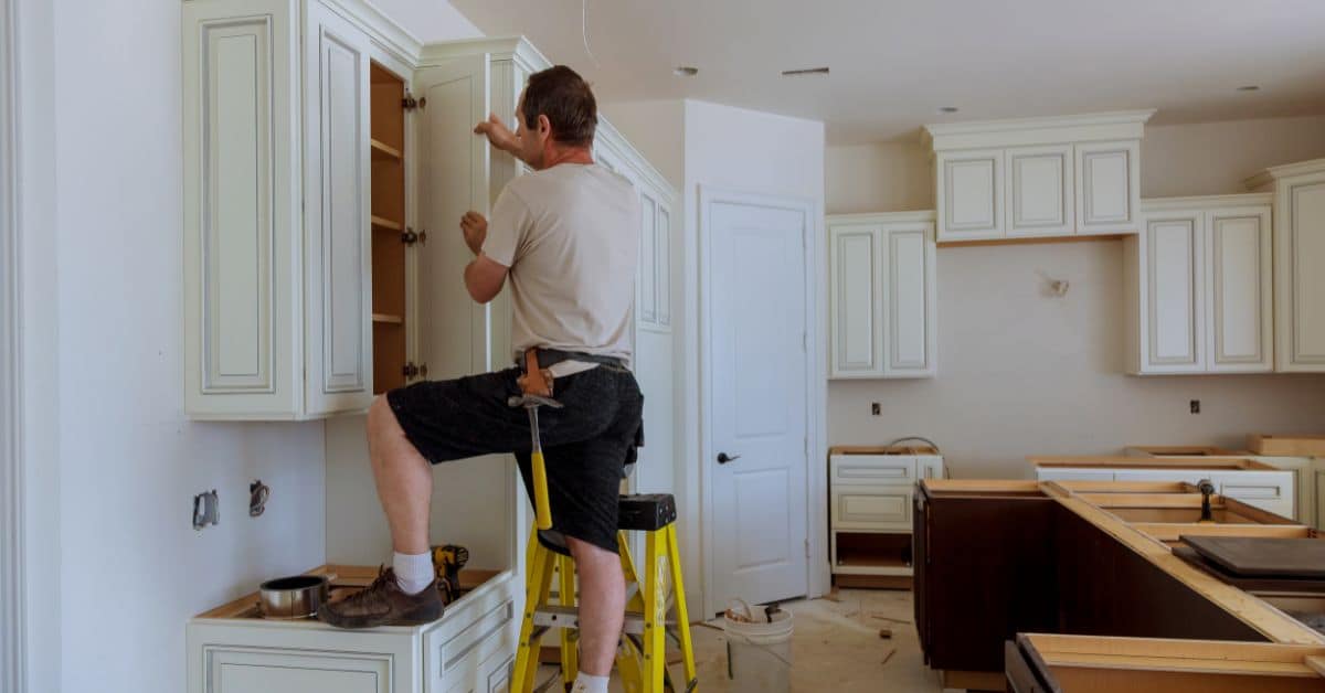Man installing kitchen cabinets during renovation process.