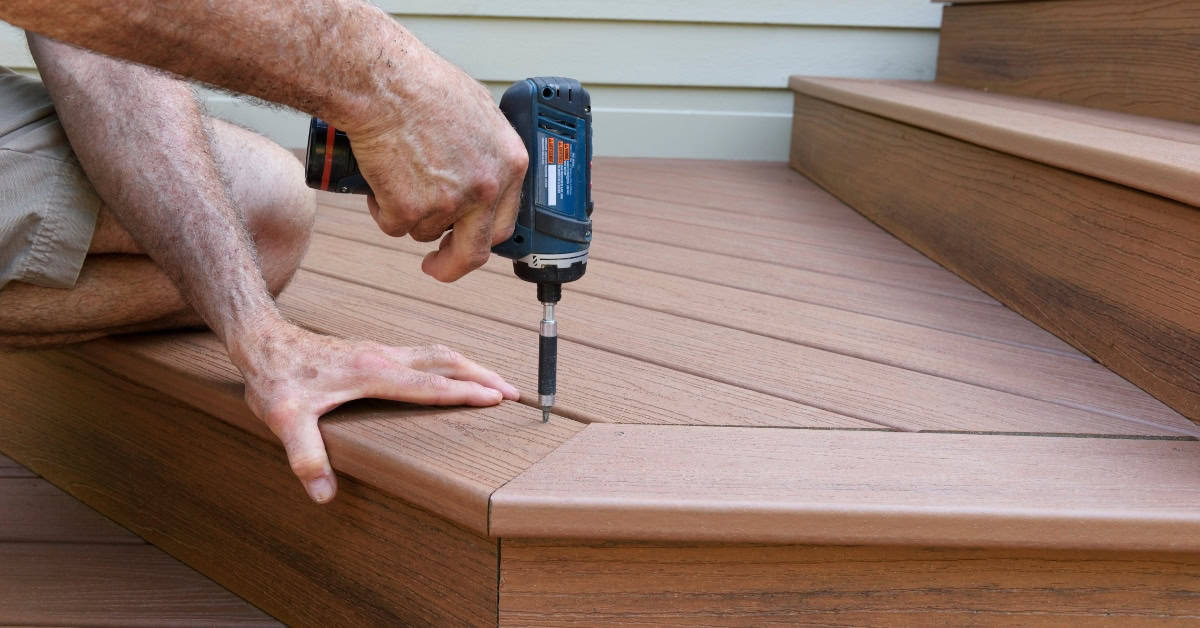 Installing composite decking on outdoor stairs with a power drill.