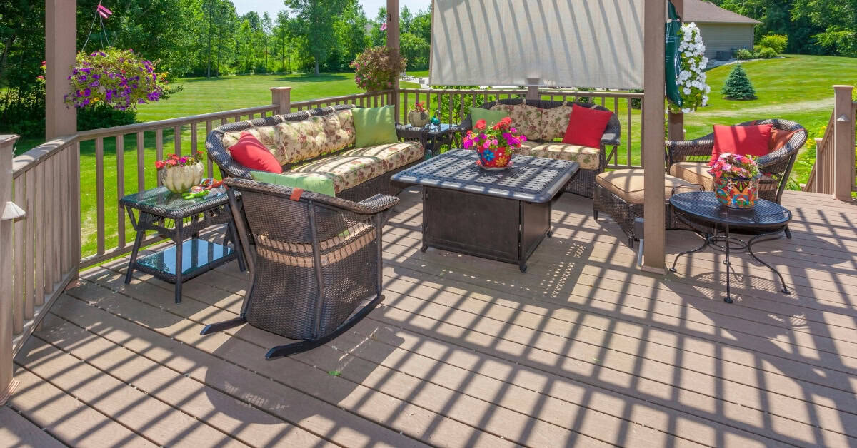 Outdoor lounge on composite decking with garden and lush greenery in the background.