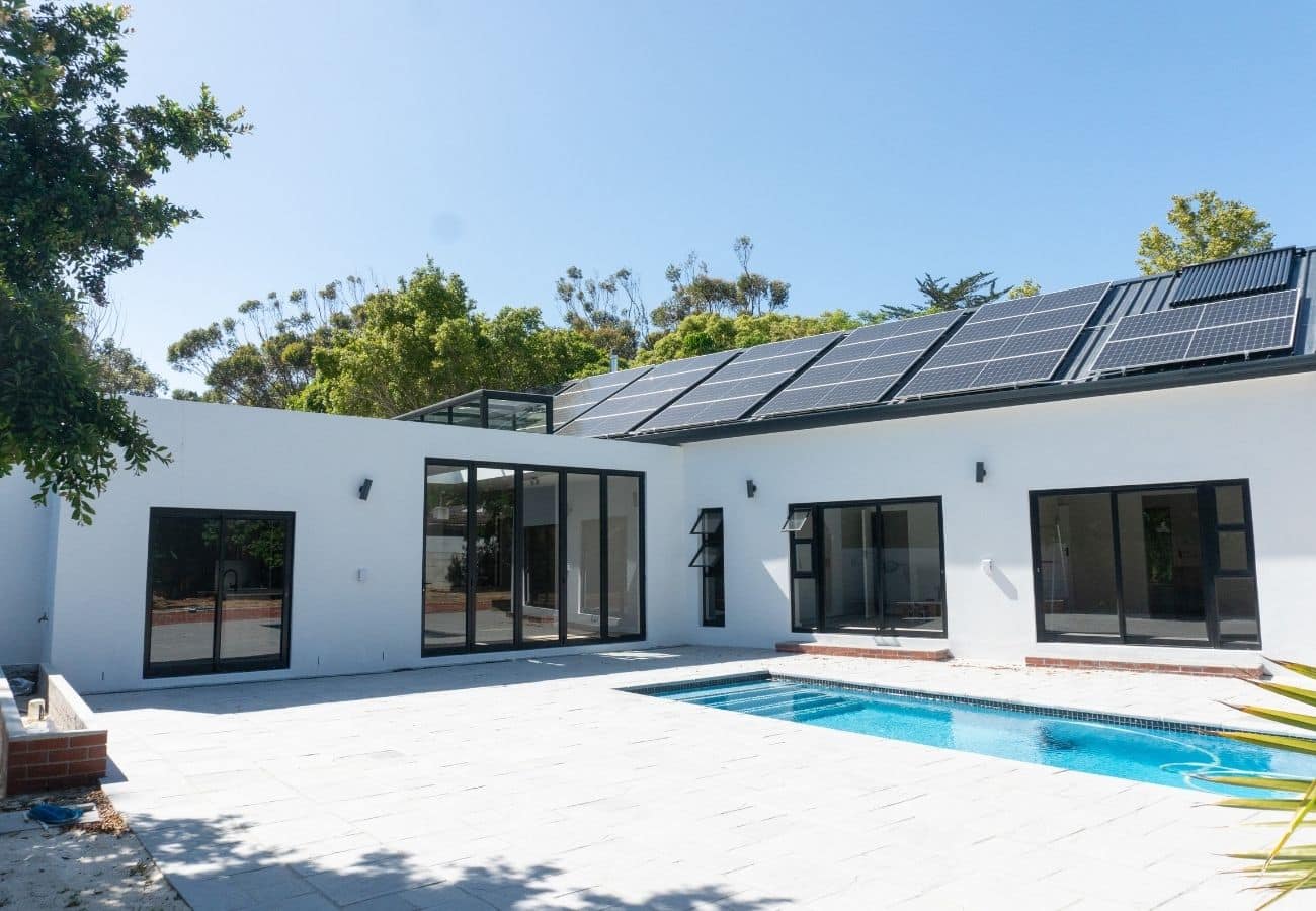 Solar panels on roof of contemporary house with pool and outdoor patio.