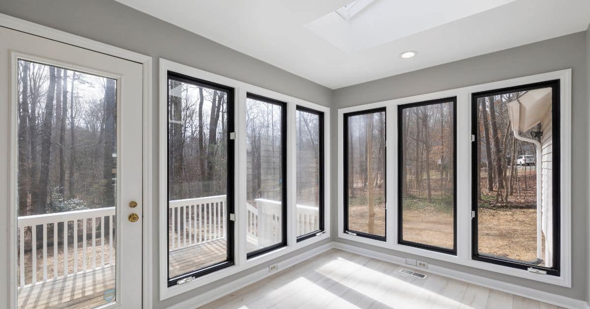 Bright sunroom with large black-framed aluminium doors and windows overlooking a wooded backyard.