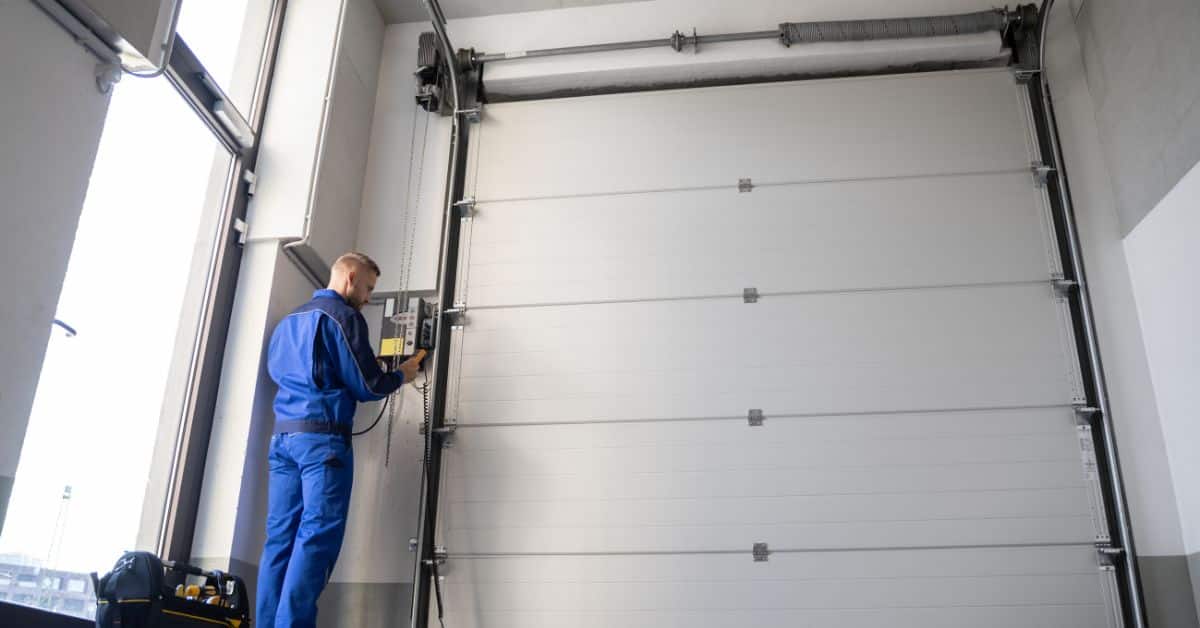 Technician installing an automatic aluminium garage door in a commercial setting.