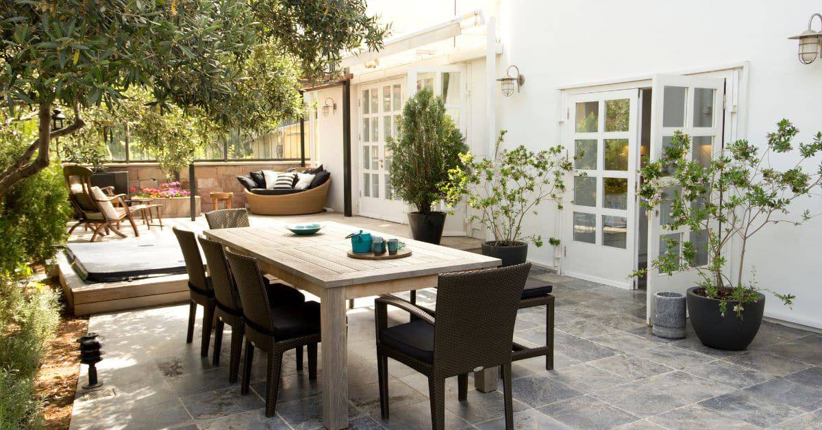 Beautiful outdoor entertainment area with dining table, lounge seating, and lush greenery.