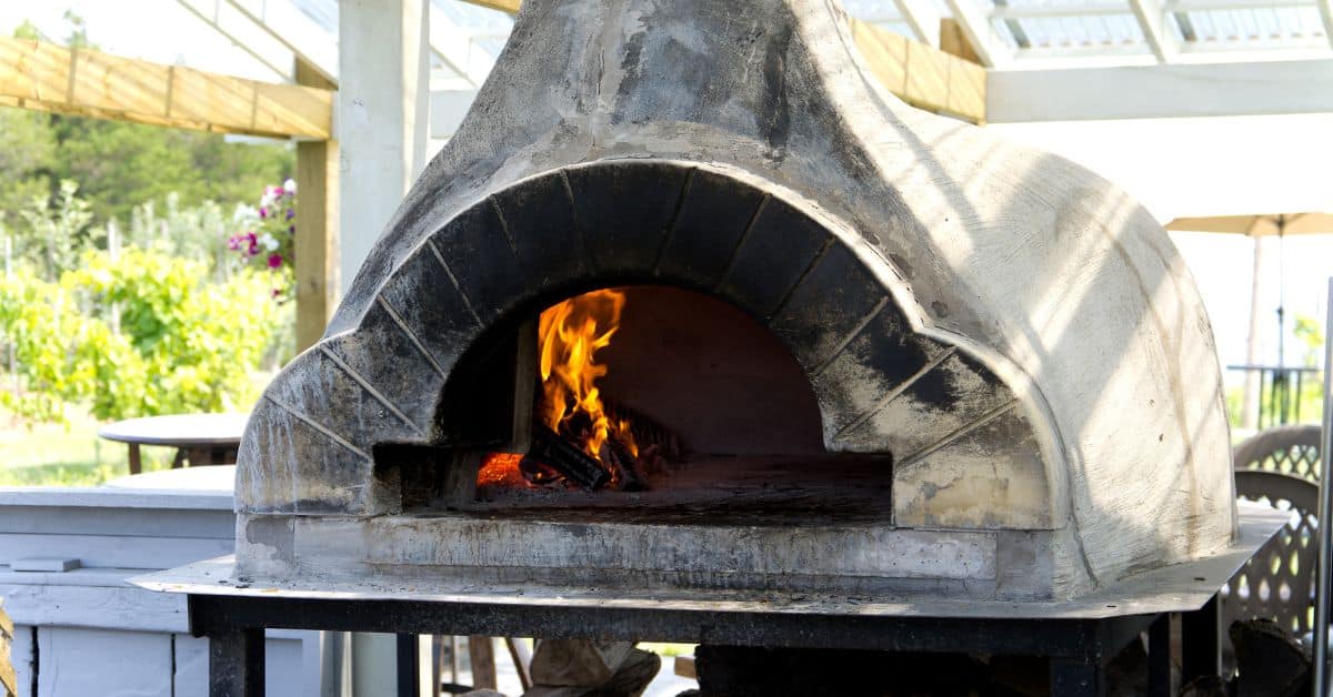 Rustic outdoor pizza oven with fire burning inside, perfect for outdoor kitchens.