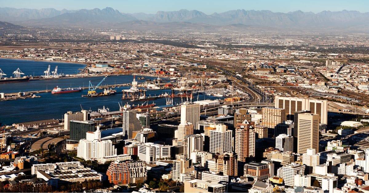 Aerial view of a bustling city with high-rise buildings, port facilities, and distant mountain range.