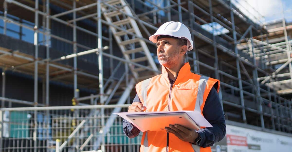 Construction site supervisor inspecting progress with scaffolding in background.