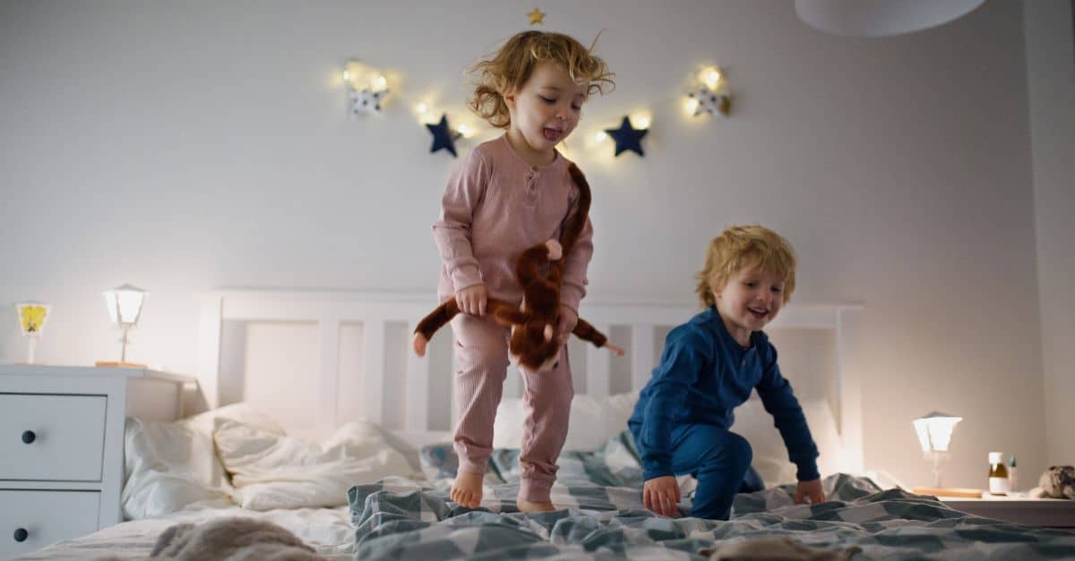 Two children playing on bed with star-shaped wall decor in a cozy bedroom.