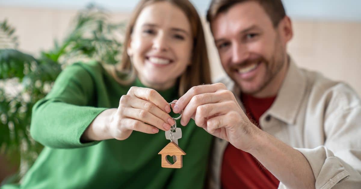 Couple smiling and holding up a key with a house keyring on it